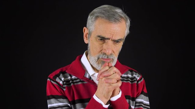 An elderly man prays with hands clasped together - black screen studio