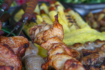 Fried meat of pig, lamb, grilled shish kebab with a delicious crust on the background of vegetables. Summer holidays and food in nature. Stock Photo.