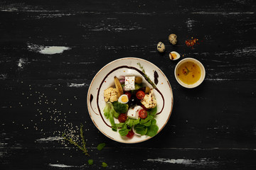 Tasty vegetarian salad made of quail eggs, lettuce, Feta cheese, broccoli, cauliflower, olives and baby corn on plate standing on blue old wooden table. Healthy dietary meal, wholesome dish. Top view.