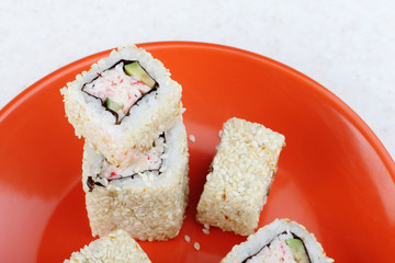 Sushi with sesame seeds on an orange plate.