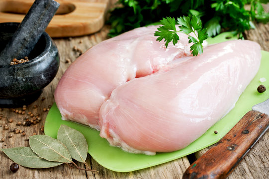 Raw chicken breast fillets on a cutting board on a wooden table with spices