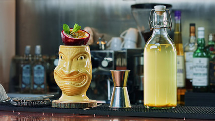Tiki cocktail with passion fruit, jigger and a bottle with tincture on the bar