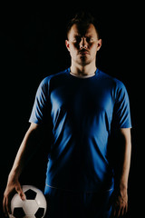 Young soccer player with ball on black background in studio.