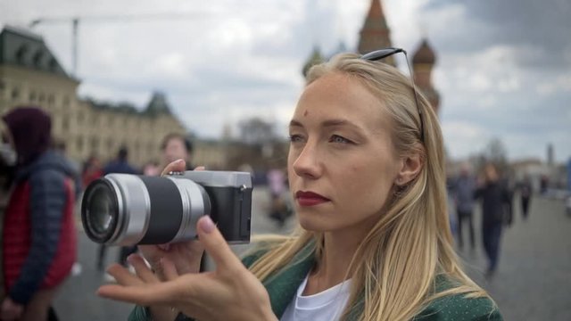 Young attractive blonde photographer woman taking off sunglasses to take pictures of the Red Square. Moscow Russia summer day. Handheld real time medium shot