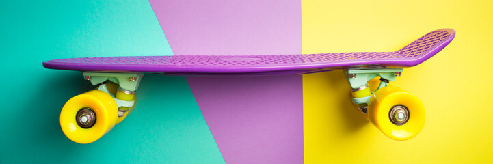 violet skateboard with yellow wheels on turquoise and purple background. plastic mini cruiser board. pastel creative concept. minimalism, flat lay, long banner