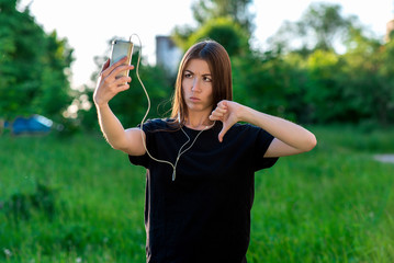 Beautiful European girl. In the summer in open air. Emotionally shows a gesture with a thumbs-down...