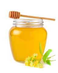 Glass jar of fresh linden honey with flowers of linden on white.