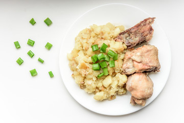Stewed potatoes with chicken and green onions on white plate.