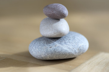 Fototapeta na wymiar Group of zen stones pile, grey meditation pebbles tower on light brown wooden background in sunlight