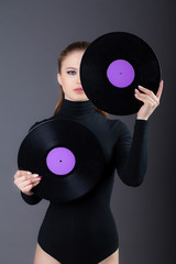 The girl is holding a vinyl disc in her hands, covering half the face. Studio shot on a gray background