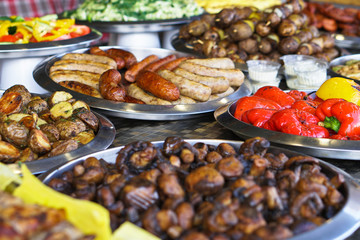 Dinner table with meat grill, roast new potatoes, vegetables, salads, sauces, snacks and lemonadeá Grilled sausage, mushrooms. Stock Photo