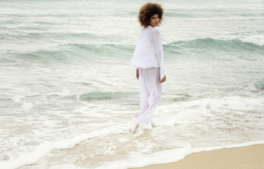 beautiful girl with afro hair and white dress walk by the sea