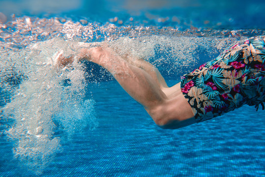 Men's legs swimming underwater in the swimming pool in summer