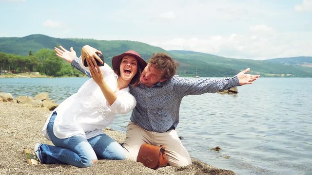 Couple in vacation taking selfie making funny pose in front of lake kissing