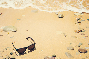Fototapeta na wymiar Sunglasses on a sandy beach with sea wave