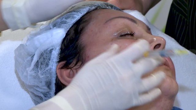 Woman gets beauty facial cosmetology procedure. Beautician hands in gloves making face aging injection in a female skin.