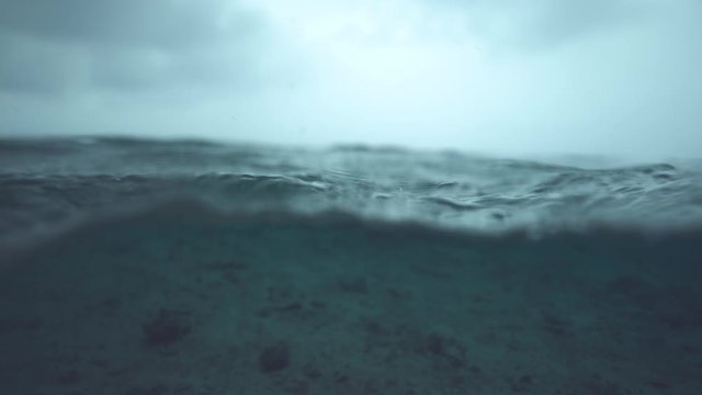 SLOW MOTION, HALF UNDERWATER, MACRO, DOF: Beautiful shot of gentle deep blue ocean waves rolling past the camera and over the empty sea floor. Tranquil sea filmed before heavy tropical rainstorm.