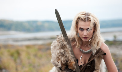 A woman warrior in the Scandinavian style of Vikings dressed in a wolf's skin is standing with a sword in his hands