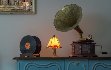 Nineteenth century phonograph (gramophone) and vinyl records on a wooden table and background of beige wall and hanged painting