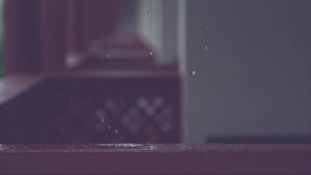 SLOW MOTION, CLOSE UP, DOF: Raindrops fall on wooden railing and splash across the empty porch in front of cool holiday apartments. Crystal clear droplets falling on brown wood surface make a ripple.