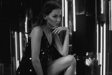Brunette woman wearing elegant black sequin strap cami dress standing on large cube. Attractive...
