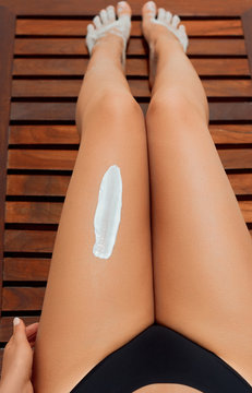 Closeup on female Hand applying sun cream on Leg. Skincare. Sun protection. Woman smear  moisturizing lotionon on her smooth tanned legs.