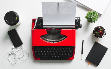 Top view of white desk workplace with bright red vintage typewriter