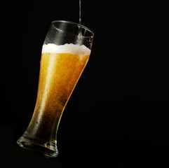 Pouring beer into glass over black background.