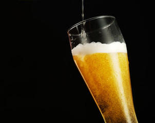 Pouring beer into glass over black background.