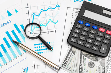Calculator with money, pen and magnifying glass on business graphs and financial documents.