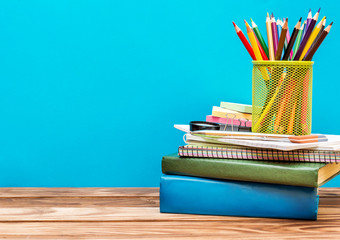 Holder with colored pencils on stack of school supplies on table against blue background. Space for text.