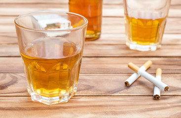 Glasses of whisky with cigarettes and bottle of whiskey on wooden background. Close up.