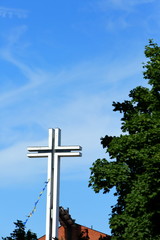 Obraz premium white big cross against the sky shining through green tree crowns.