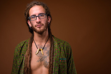 Young handsome Hispanic man with dreadlocks against brown backgr