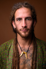 Young handsome Hispanic man with dreadlocks against brown backgr