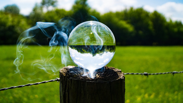 Photo Spere crystal ball reflecting and magnifying sun beams to burn fence post with countryside screne reflected upside down in ball