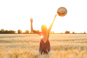 girl in a field on a sunset background throws a hat in the sky.