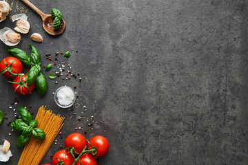 Essenshintergrund für leckere italienische Gerichte mit Tomate. Verschiedene Kochzutaten mit Spaghetti und Löffel. Draufsicht mit Kopierbereich.