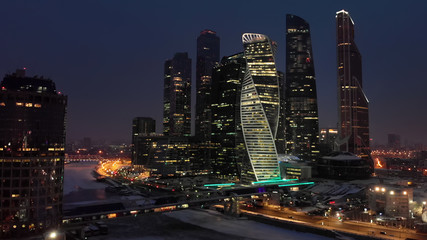 Night aerial shot of Moscow-city business towers with illuminated windows and Bagration bridge over the frozen river Moskva.