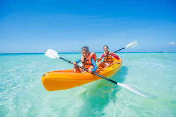 Happy boy and girl kayaking at tropical sea on yellow kayak - obrazy, fototapety, plakaty