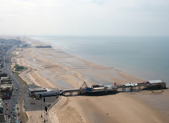 aerial view of blackpool looking north showing the beach at low tide with famous piers and the roads and buildings of the town stretching down the coast to the irish sea on the horizon