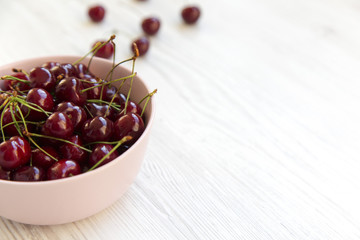 Fresh sweet cherries in a pink bowl on white wooden background. Side view. Copy space.