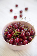 Sweet cherries in a pink bowl on white wooden table. Side view. Closeup.