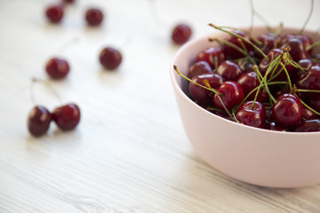 Fresh cherries in a pink bowl on white wooden background. Side view. Closeup.