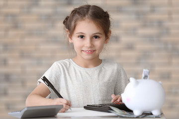 Cute little girl counting money at table