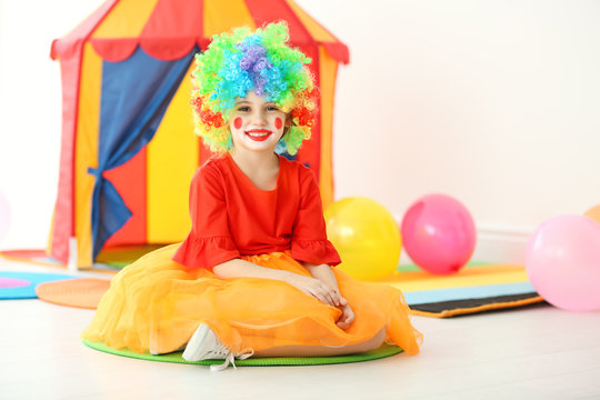 Cute little girl with clown makeup in carnival costume indoors. April fool's day celebration