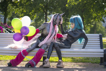 funny freaks, dressed in a unicorn bright costume and anime face mask with latex catsuit, enjoy life in the city Park