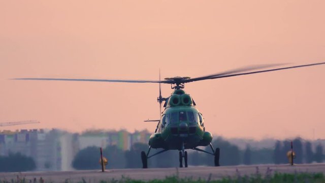 Military helicopter takes off from the airfield at sunset