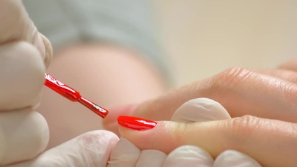 Detail of covering finger nails with varnish. Close up manicurist in white gloves applying red nail polish to client. Classic color manicure.
