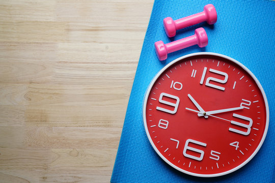 Time for exercising clock and dumbbell on yoga mat background, sport and healthy concept